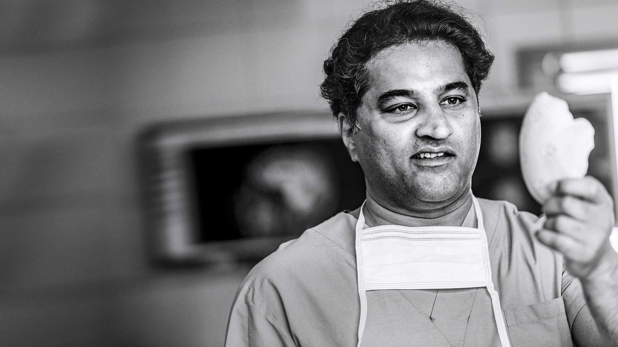 Chirurg mit OP-Maske um den Hals betrachtet ein PEEK Schädelimplantat